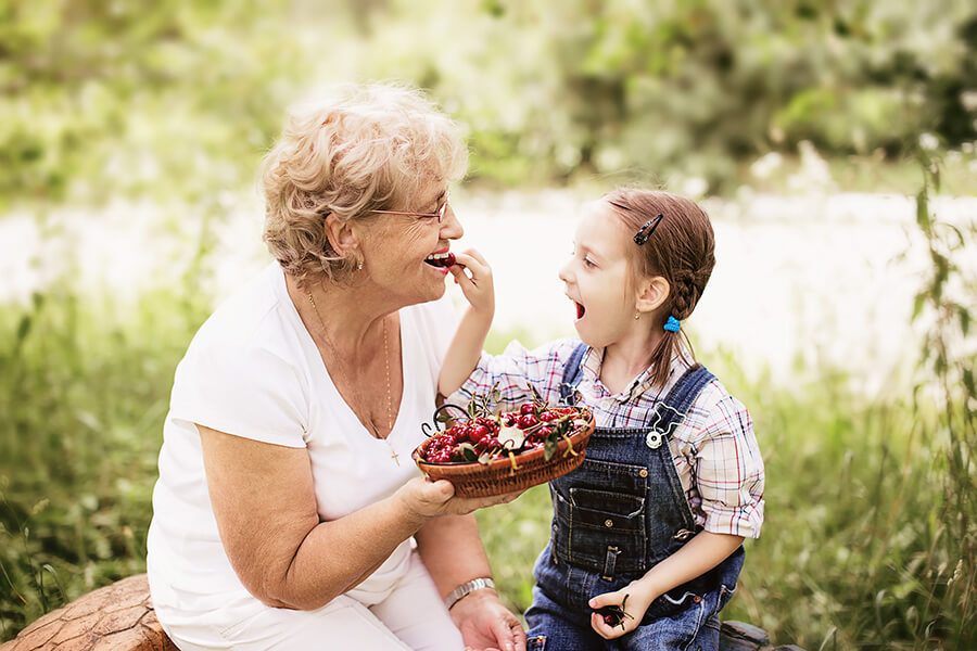 A young girl feeding her happy mother some cherries on a picnic